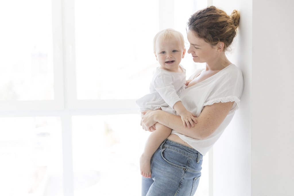 Женщина с ребенком светлый фон. Мать держит на коленях детей. August mama.